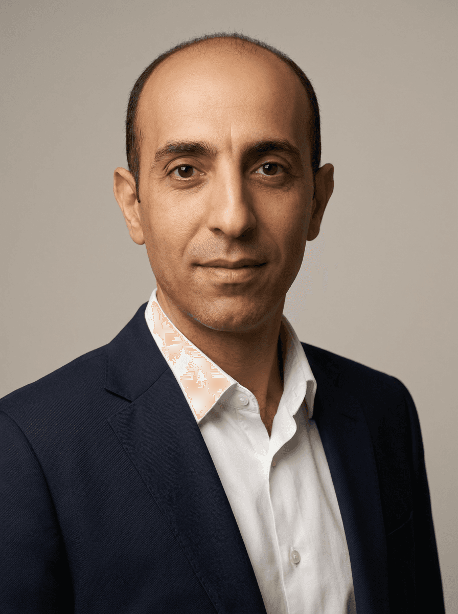 Example studio headshot of a man, mid 30s, Middle Eastern, a navy suit jacket over a white shirt, no tie, on a light-grey backdrop